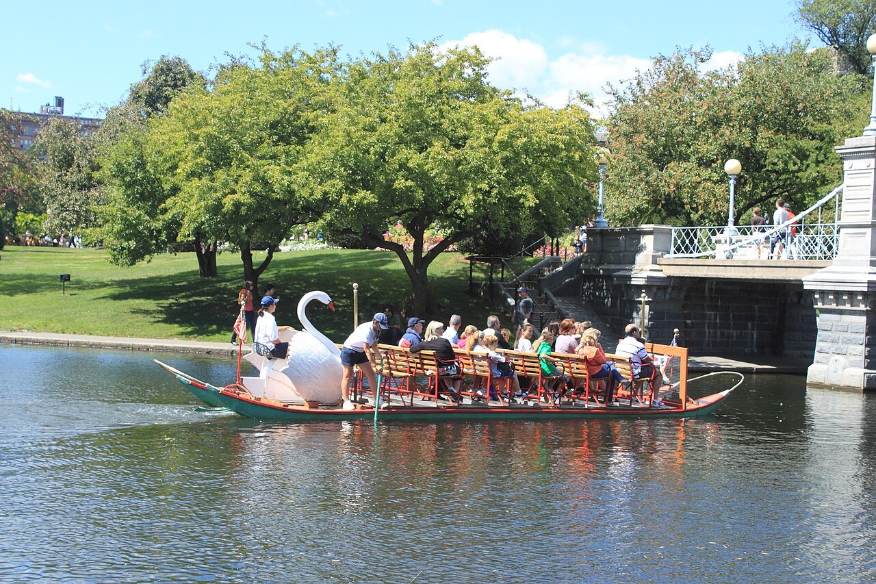 A Swan Boat, its pedaler hidden behind the swan, passing the lagoon bridge