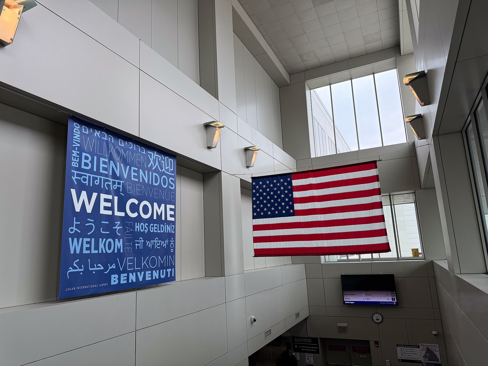 A welcome sign in many languages beside the flag in Logan's arrivals hall