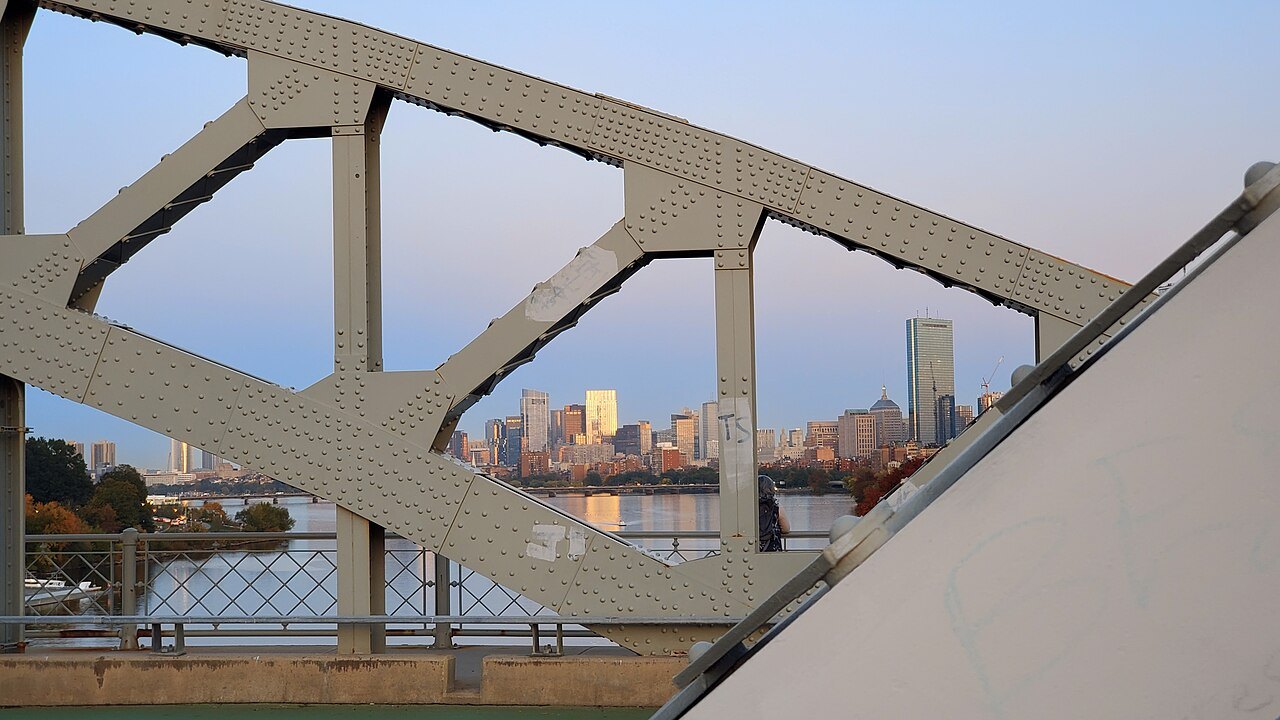 The steel truss of the Boston University Bridge framing the city at dusk
