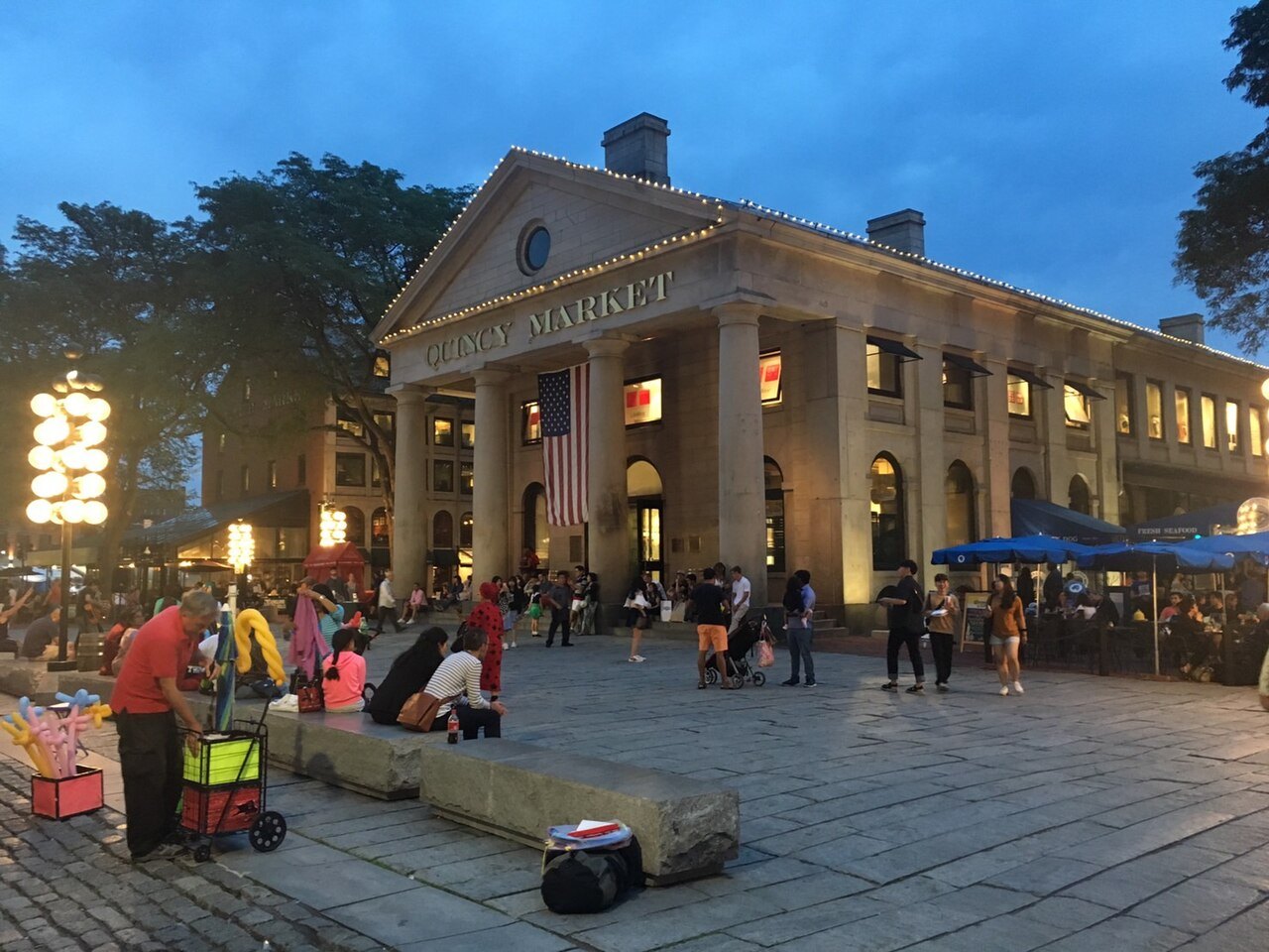The columned front of Quincy Market lit at dusk, people gathered on the plaza