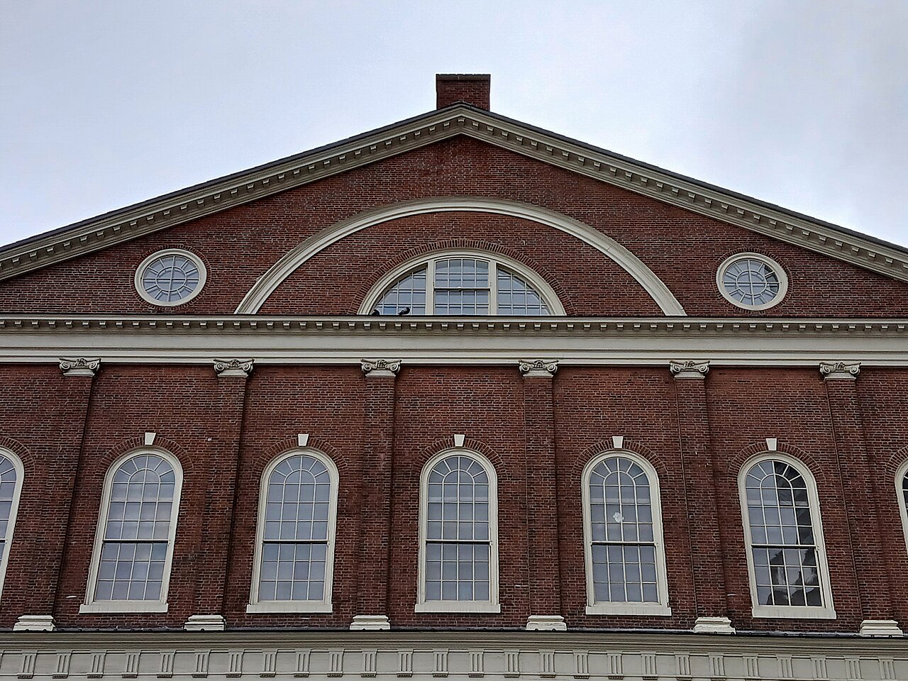 The pediment and round window above the arched upper windows of Faneuil Hall