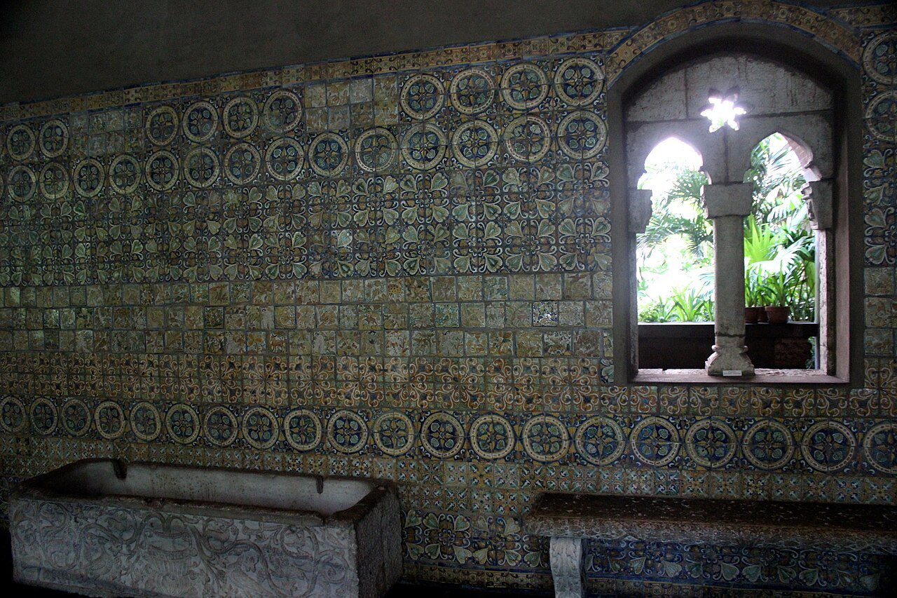 A wall of old patterned tiles around a stone window in one of the palace's cloisters