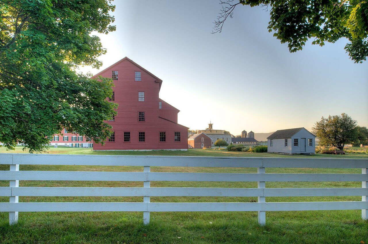 A white board fence before a red Shaker building in low morning light