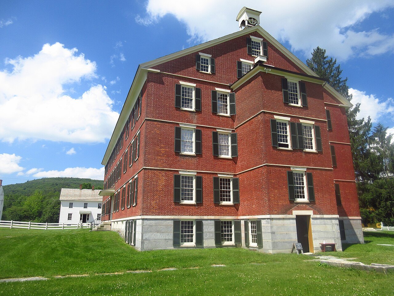 A tall red-brick Shaker building with rows of shuttered windows