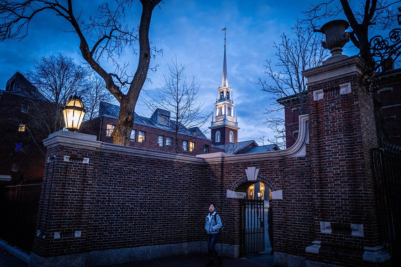 A brick gate of Harvard Yard at dusk, the white steeple of Memorial Church beyond