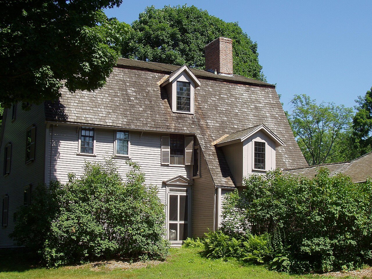 The Old Manse seen from the Concord River, its gray clapboard behind the shrubs
