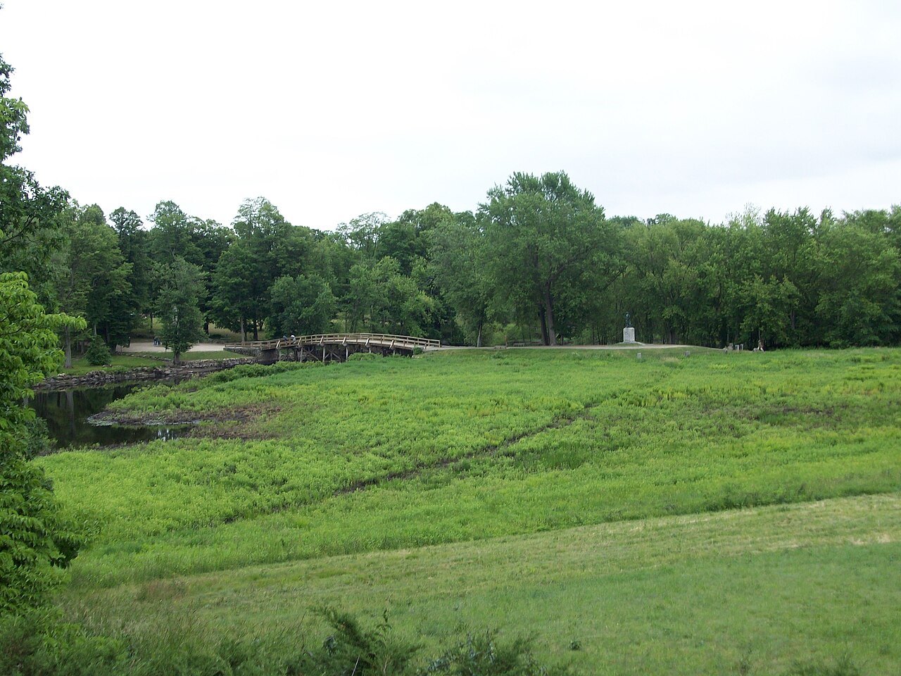 The North Bridge beyond a green meadow along the Concord River