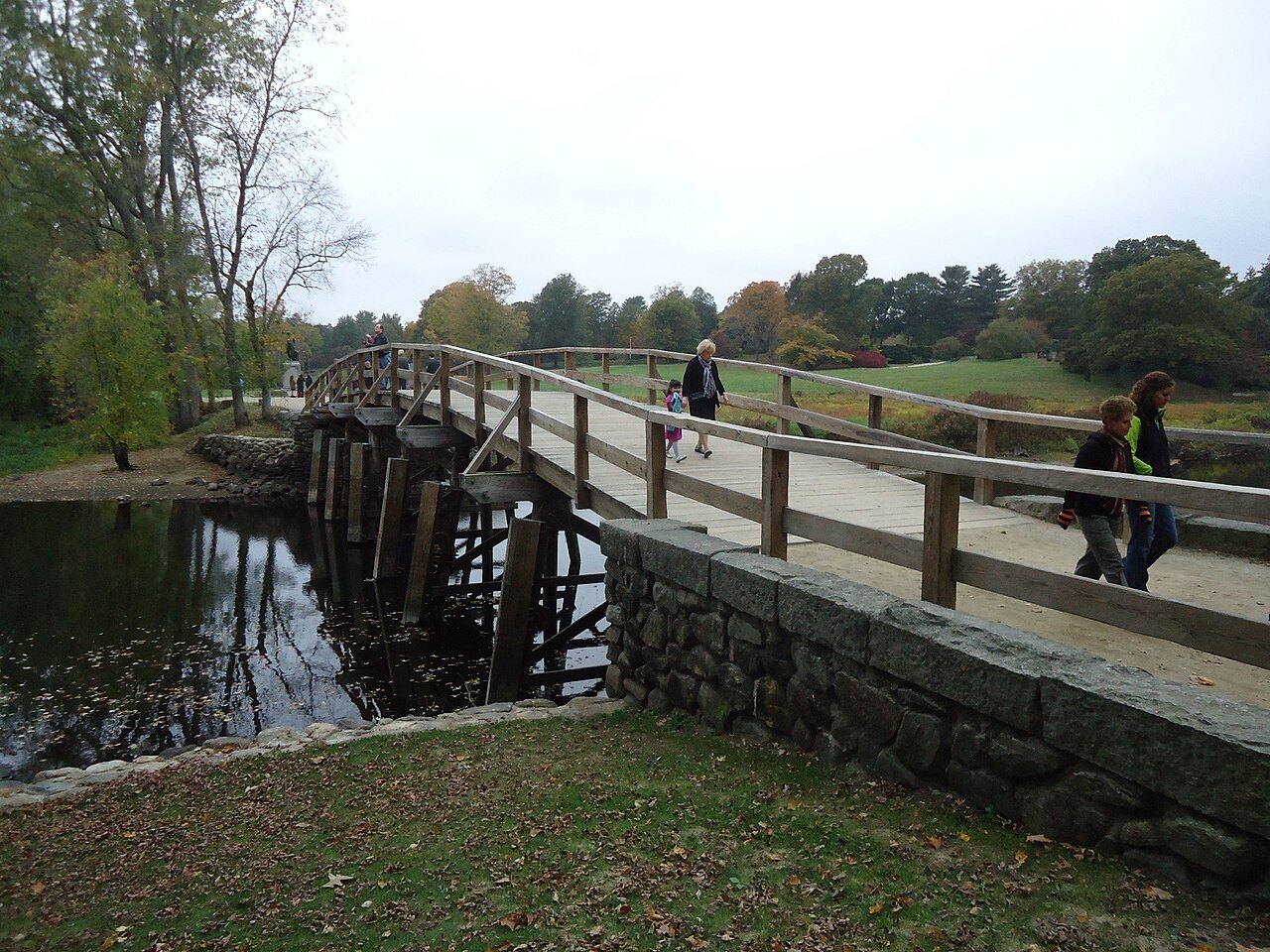 Visitors crossing the North Bridge above the still water of the Concord River
