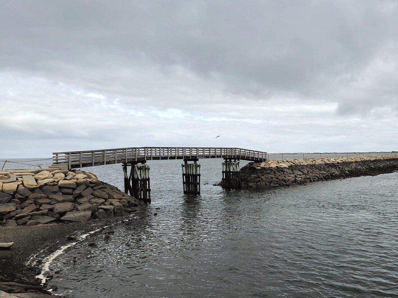 A wooden footbridge on the harbor jetty under a gray sky