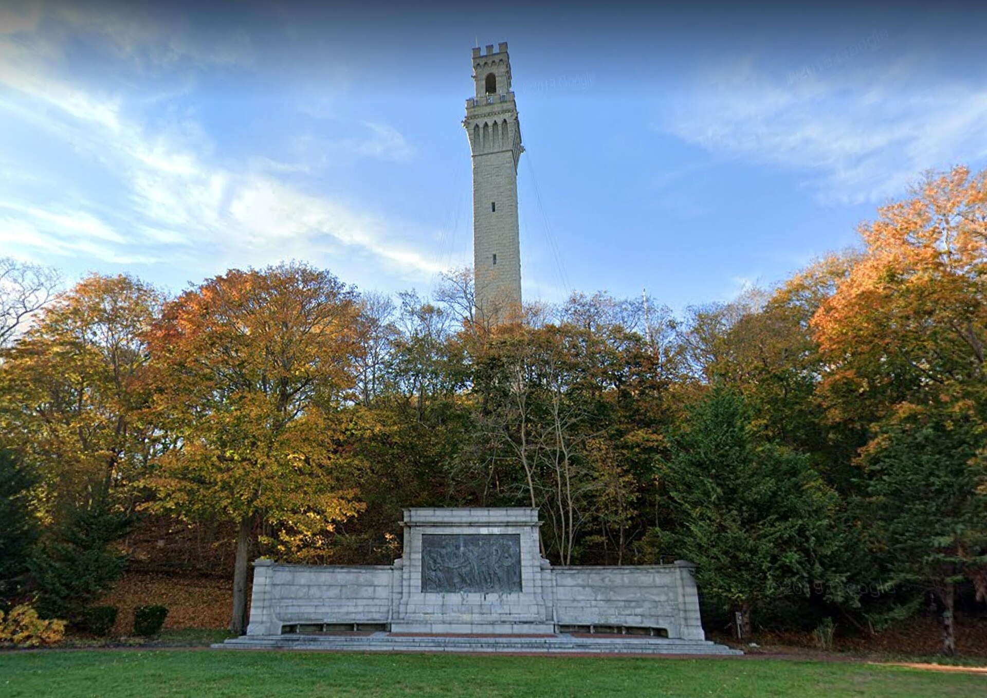 The granite tower of the Pilgrim Monument above autumn trees, the bas-relief memorial below