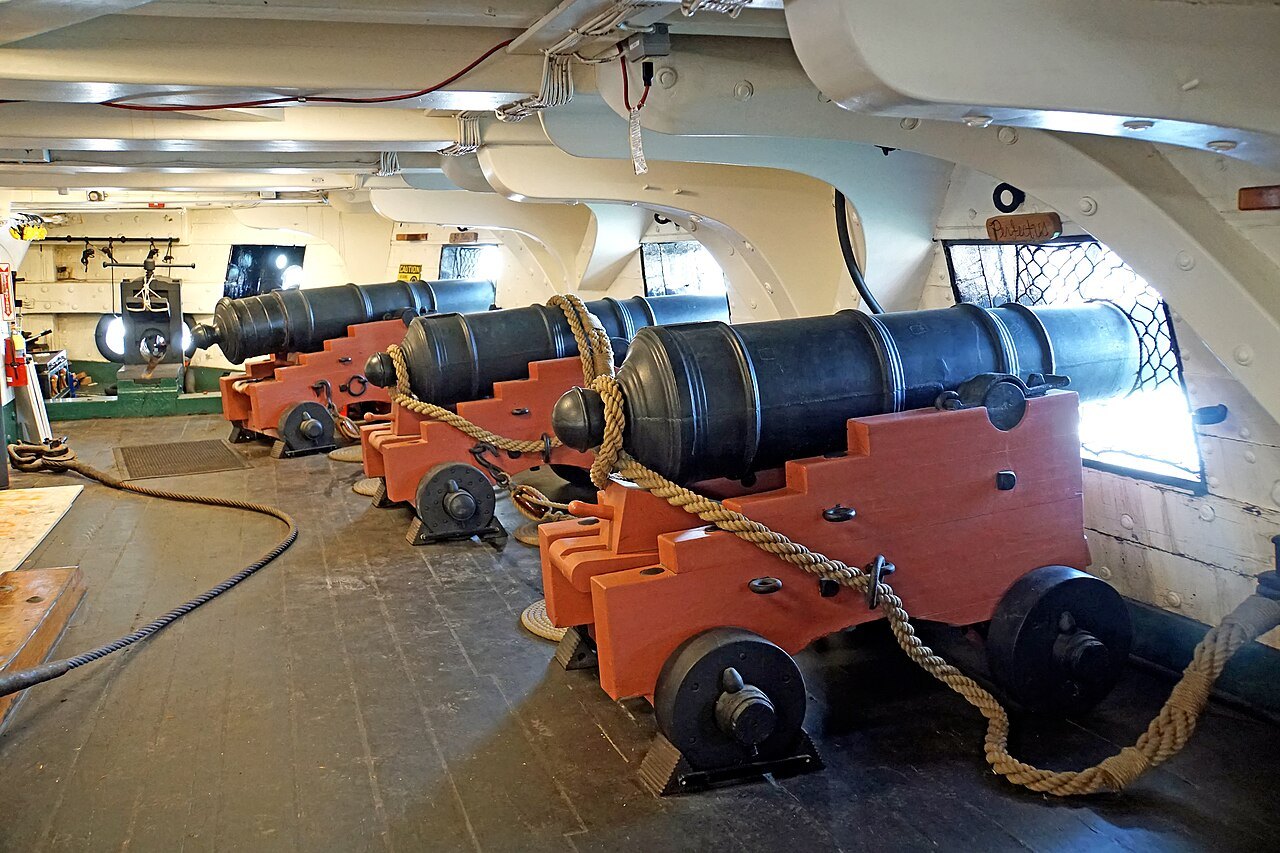 The gun deck, its long guns on red carriages run out to the ports