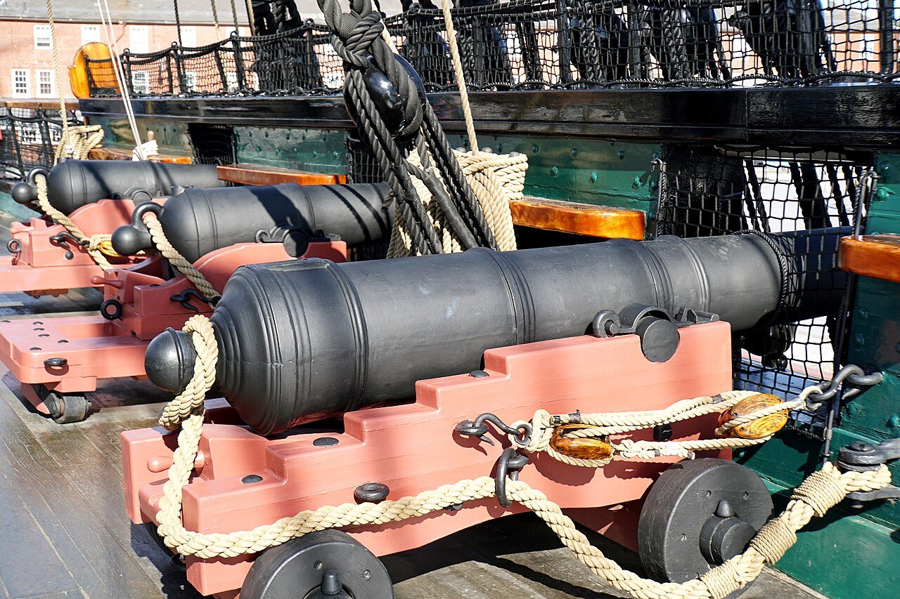 A long gun on the spar deck, lashed with rope to its red carriage