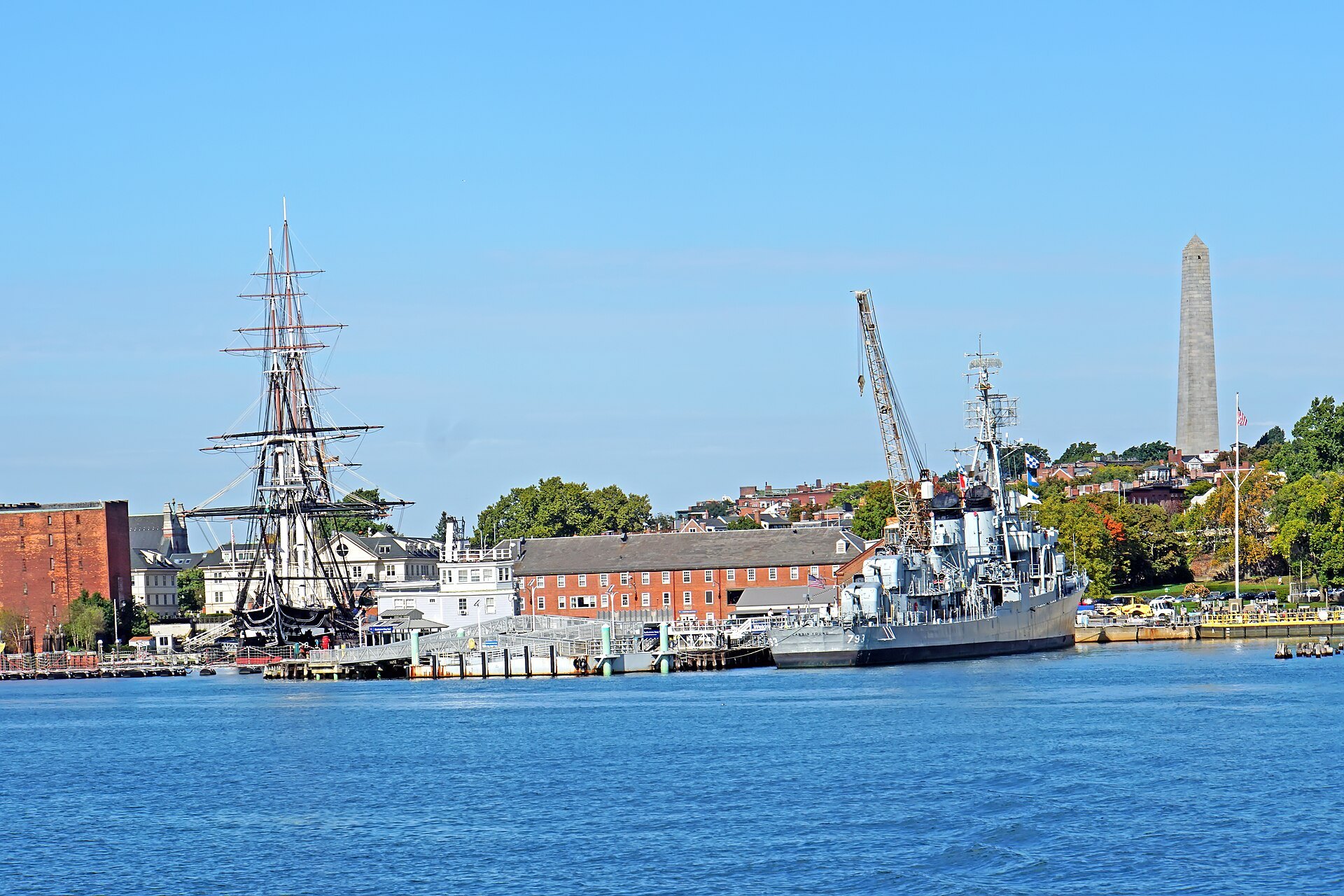 USS Constitution at her pier in the Charlestown Navy Yard, the Bunker Hill Monument on the hill behind