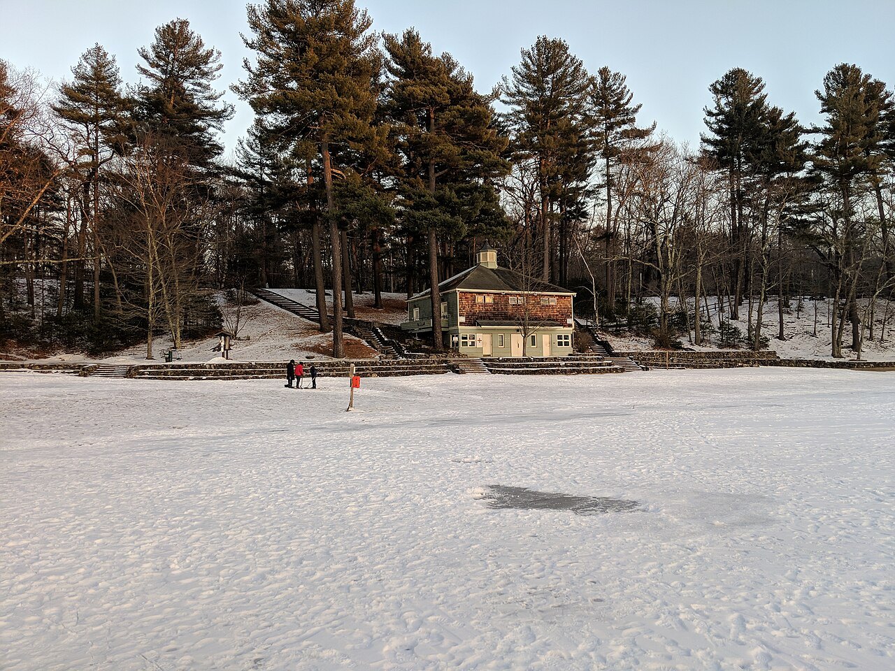 The pond frozen under snow in winter, the bathhouse among the pines